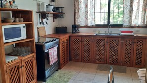 Une cuisine de taille réduite équipée d’un four à micro-ondes, d’une cuisinière et de meubles de rangement en bois.