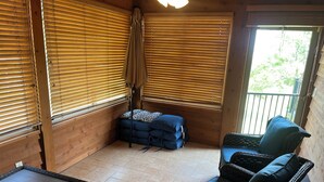 Una habitación acogedora con paredes de madera, suelo de baldosas y un balcón con mobiliario de mimbre y cojines azules.