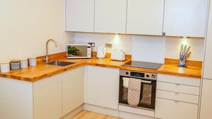 A modern kitchen with white cabinets, a wooden countertop, a built-in oven, and a coffee maker. - Shrewsbury Modern 1 Bedroom Flat By Bevolve (Shrewsbury)