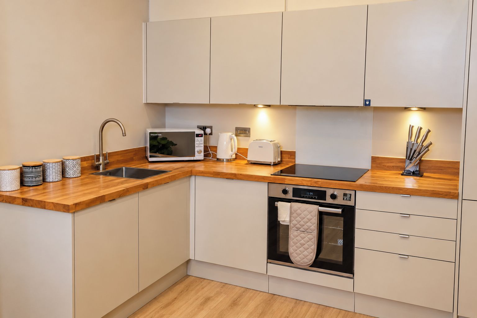 A modern kitchen with a wooden countertop, a built-in oven, a microwave, and a sink.