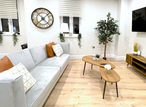A modern living room with a white sofa, a wooden coffee table, and a large wall clock. - Shrewsbury  Modern 1 Bedroom Flat By Bevolve (Shrewsbury)