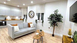 A modern living room with a grey sofa, wooden coffee table, and a large plant.