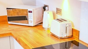 A kitchenette with a microwave, toaster, and kettle on a wooden countertop.
