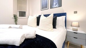 A neatly made bed with white and dark blue bedding, a bedside table with a lamp, and two framed pictures on the wall.