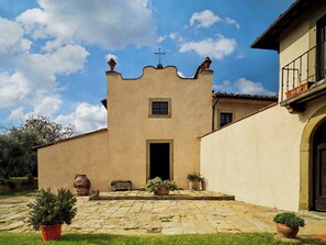 Ein Innenhof mit Steinpflaster, Blumentöpfen und einem Gebäude mit schlichter Fassade und einem kleinen Fenster.
