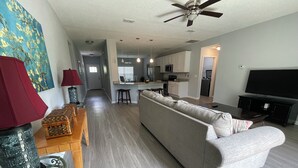 Un salon moderne avec un canapé gris, une lampe rouge, une table basse en verre et un ventilateur de plafond.