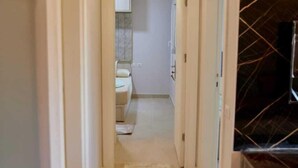 A narrow hallway with a light-colored carpet leading to a bathroom with a toilet and sink. - Long Island Chalets Family only (Marsa Matrouh)