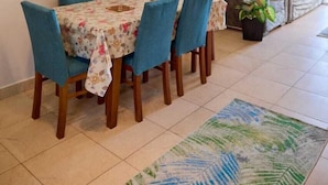 A dining area with a table set for four, blue chairs, and a floral tablecloth. There is a sofa with cushions in the background. - Long Island Chalets Family only (Marsa Matrouh)