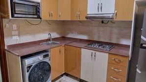 A compact kitchen with a built-in microwave, a gas stove, a washing machine, and wooden cabinets. - Long Island Chalets Family only (Marsa Matrouh)