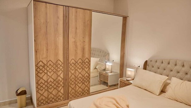 A bedroom with a large wardrobe, a bed with a beige blanket, and bedside lamps. - Long Island Chalets Family only (Marsa Matrouh)