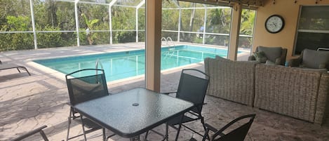 A covered outdoor area with a pool, seating, and a clock on the wall.
