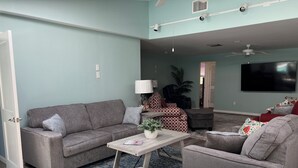 A spacious living room with a grey sofa, a coffee table, and a TV mounted on the wall. - Spacious 4-bedroom house with WiFi, AC in charming Sanibel (Sanibel)