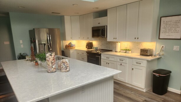 A modern kitchen with white cabinetry, a large island, stainless steel appliances, and a wooden floor. - Spacious 4-bedroom house with WiFi, AC in charming Sanibel (Sanibel)