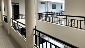 Un couloir à plusieurs niveaux, aux murs blancs et aux rampes noires, agrémenté de colonnes et doté d’un plafond avec des puits de lumière.