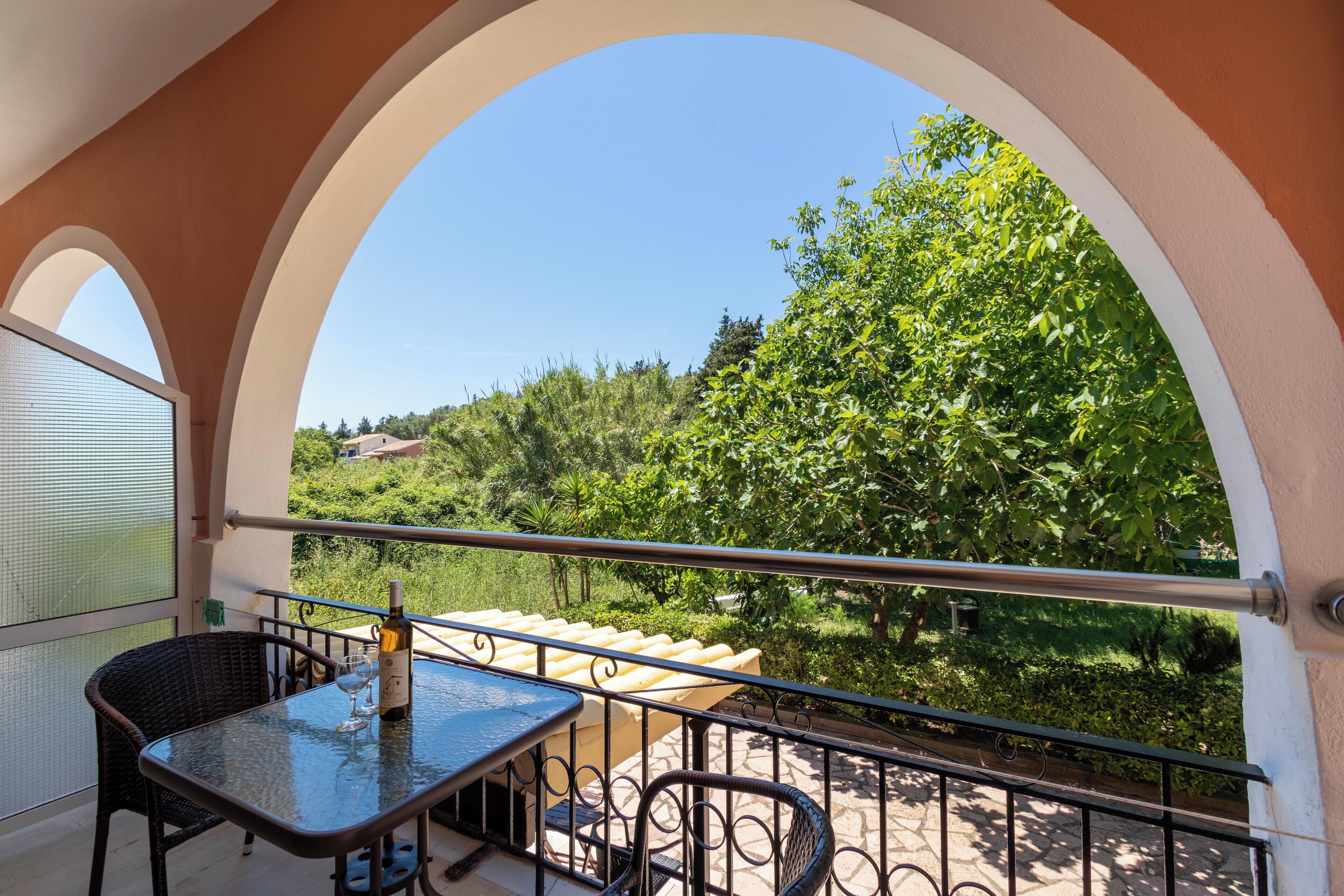Un balcon avec une table et des chaises, une bouteille de vin et une vue sur la verdure et les collines.