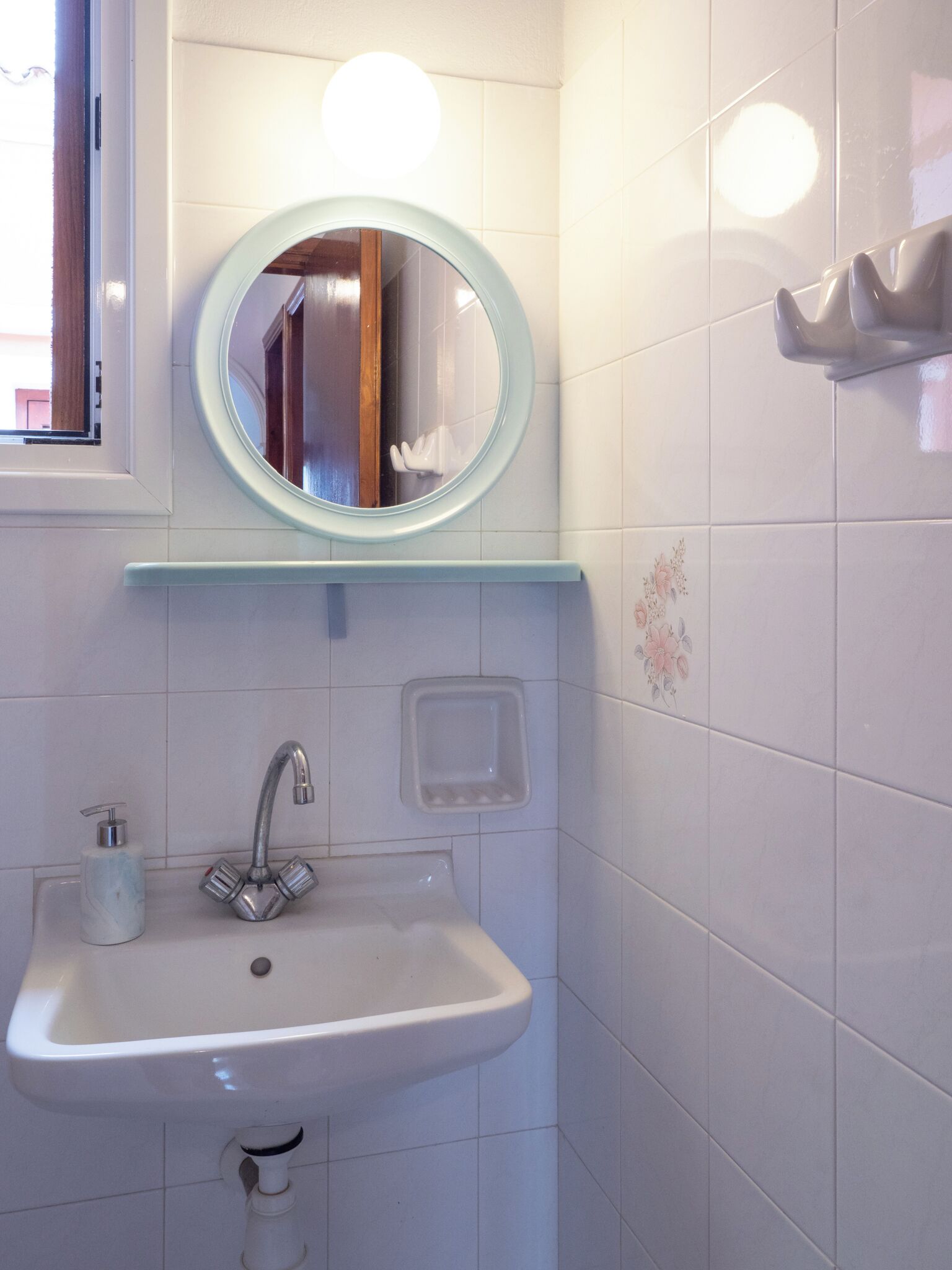Un baño con un lavamanos blanco, un espejo y un dispensador de jabón.