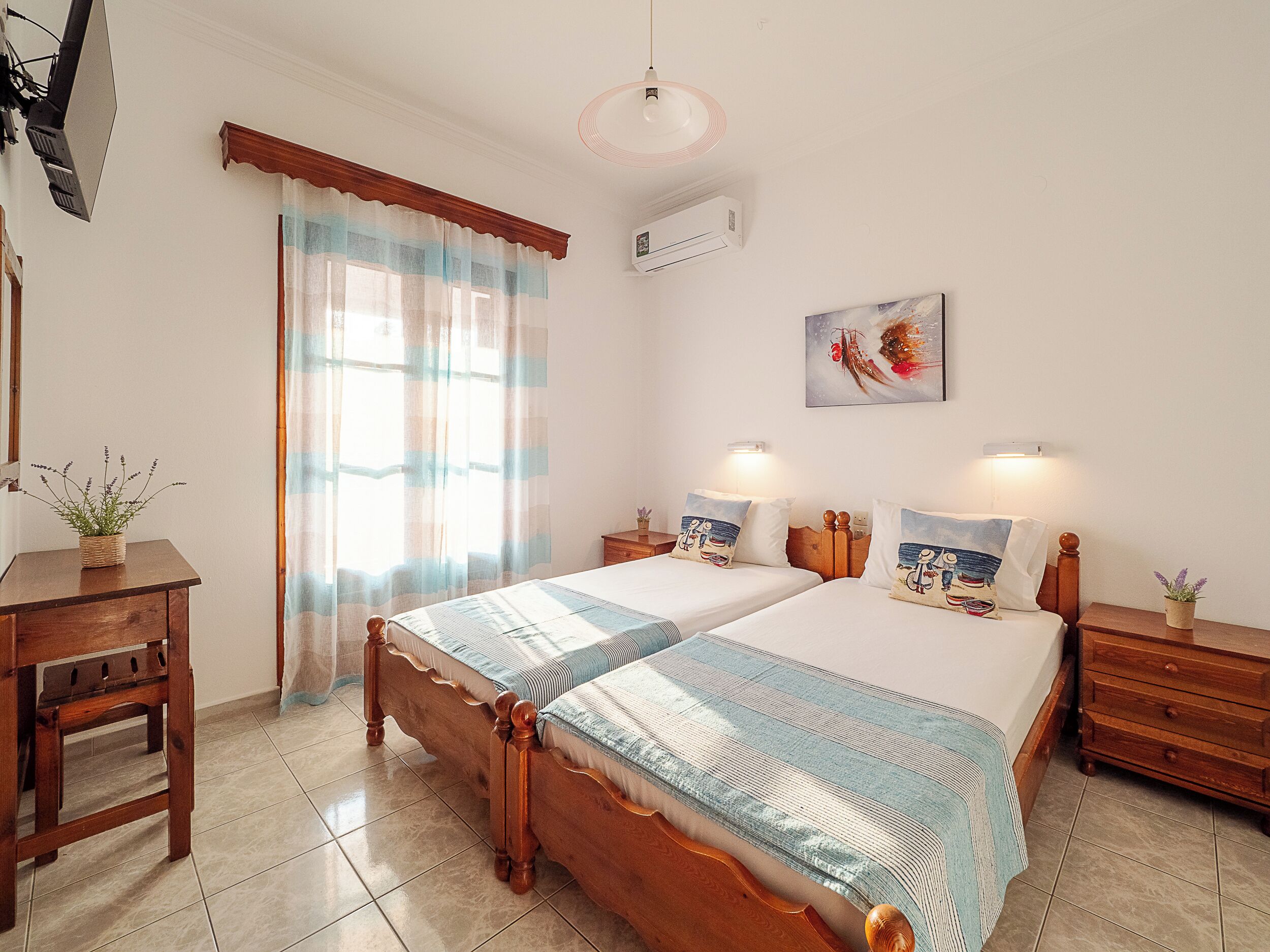 Une chambre avec deux lits, une commode en bois, une table de chevet, une plante en pot et un climatiseur fixé au mur.