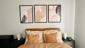 Ein Schlafzimmer mit einem Bett, zwei Nachttischen und drei gerahmten abstrakten Kunstwerken an der Wand.