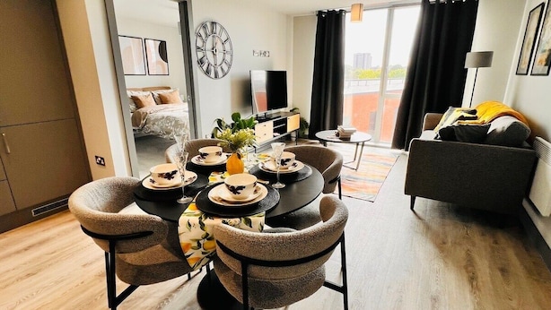 Ein modernes Wohnzimmer mit Essbereich, einer Couch, einem Fernseher und einem großen Fenster mit Vorhängen.