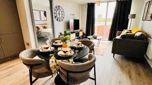 Ein modernes Wohnzimmer mit Essbereich, einer Couch, einem Fernseher und einem großen Fenster mit Vorhängen.