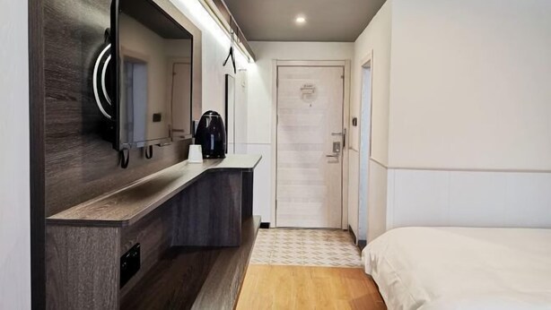 A modern hotel room with a dark wood vanity, a large mirror, a coffee maker, a bed with white bedding, and a patterned rug. - Shanghai Jinrui Hotei （Linyi Road ） (Shanghai)