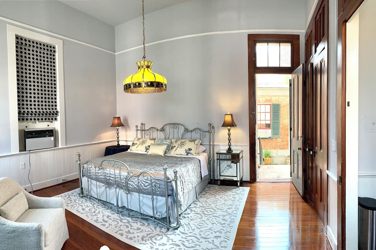 Un dormitorio con cama, mesitas de noche, una silla, un tapete estampado y una lámpara colgante.
