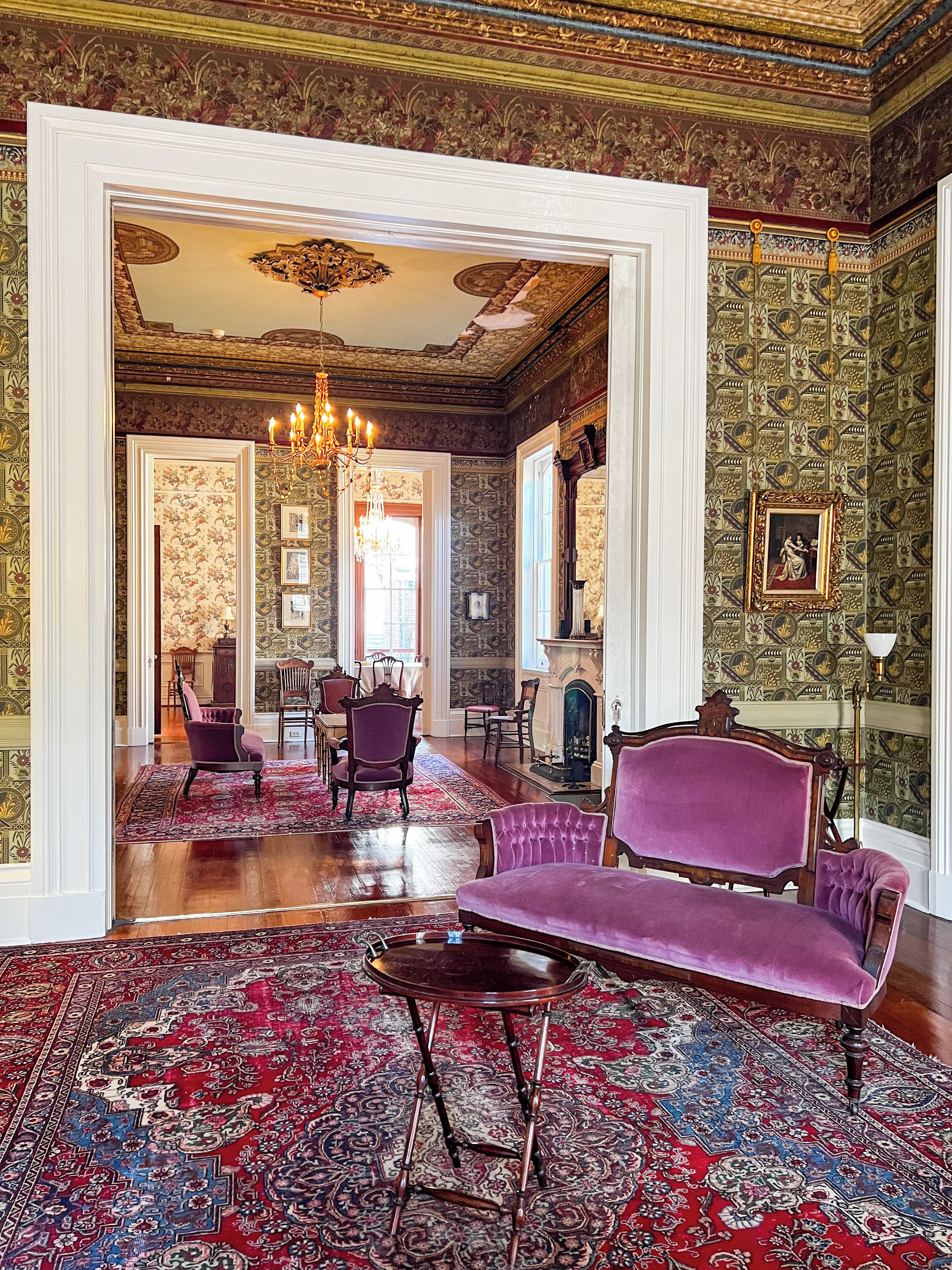 A grand room with a large chandelier, ornate wallpaper, and a purple sofa.