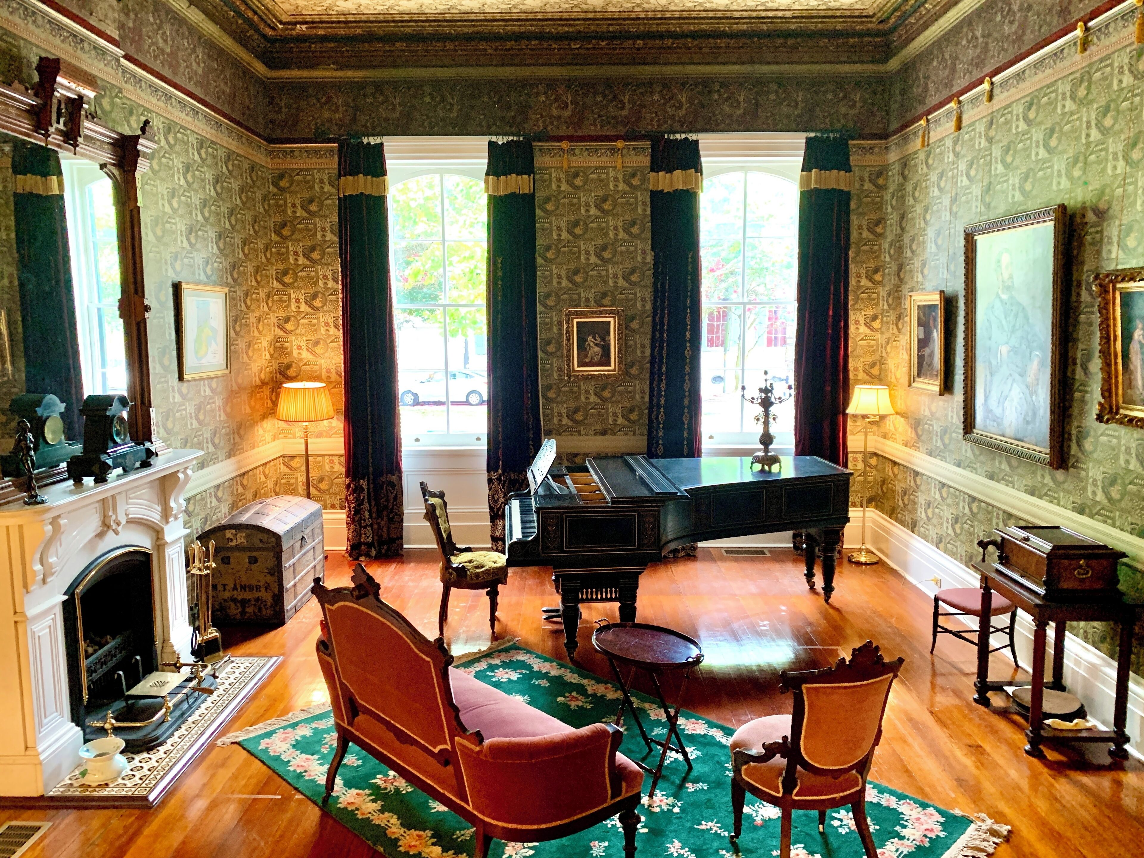 A room with a grand piano, a fireplace, and a large window with curtains.