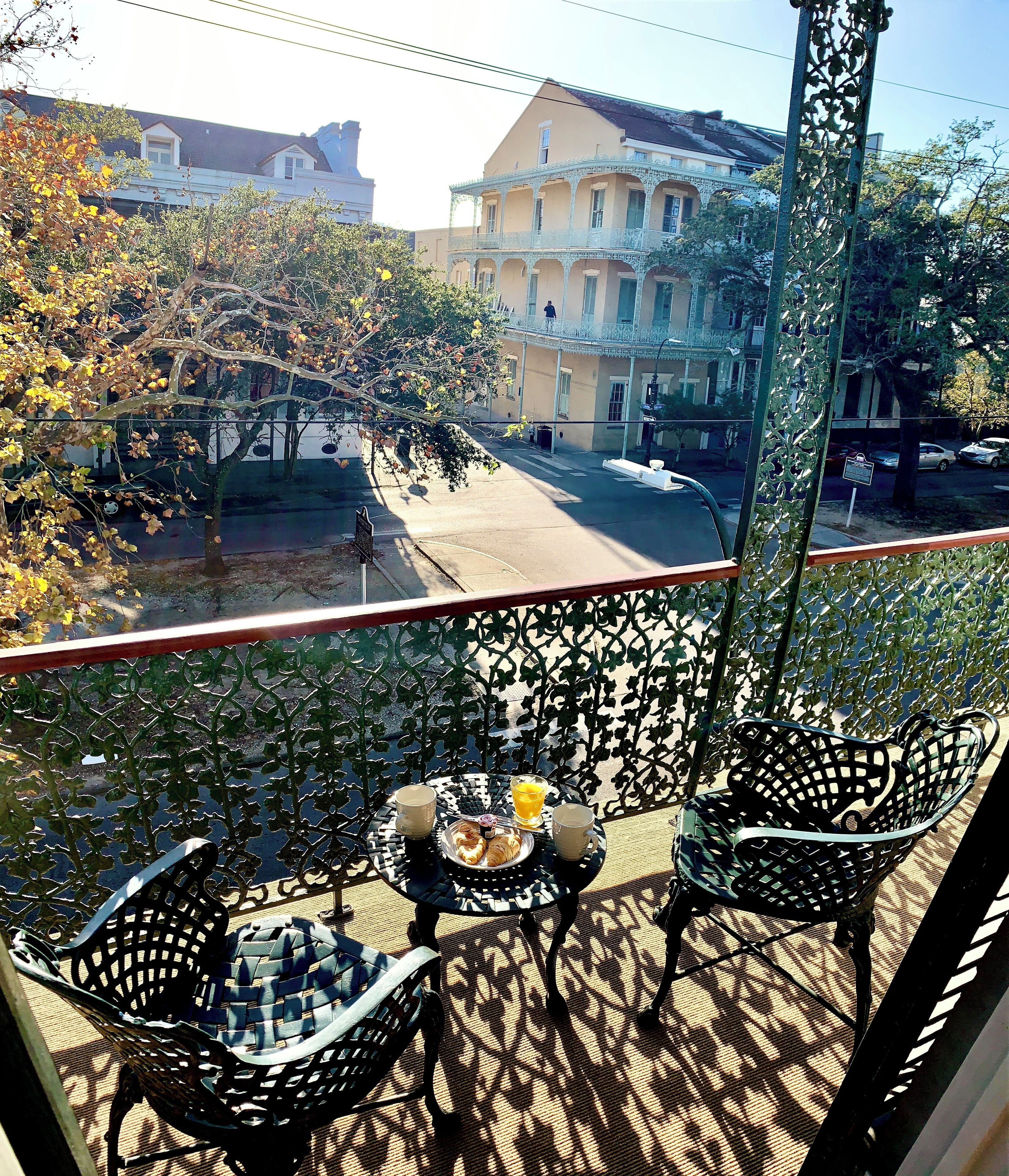 Un balcon avec une table dressée pour le petit-déjeuner, donnant sur une rue bordée d’immeubles et d’arbres.