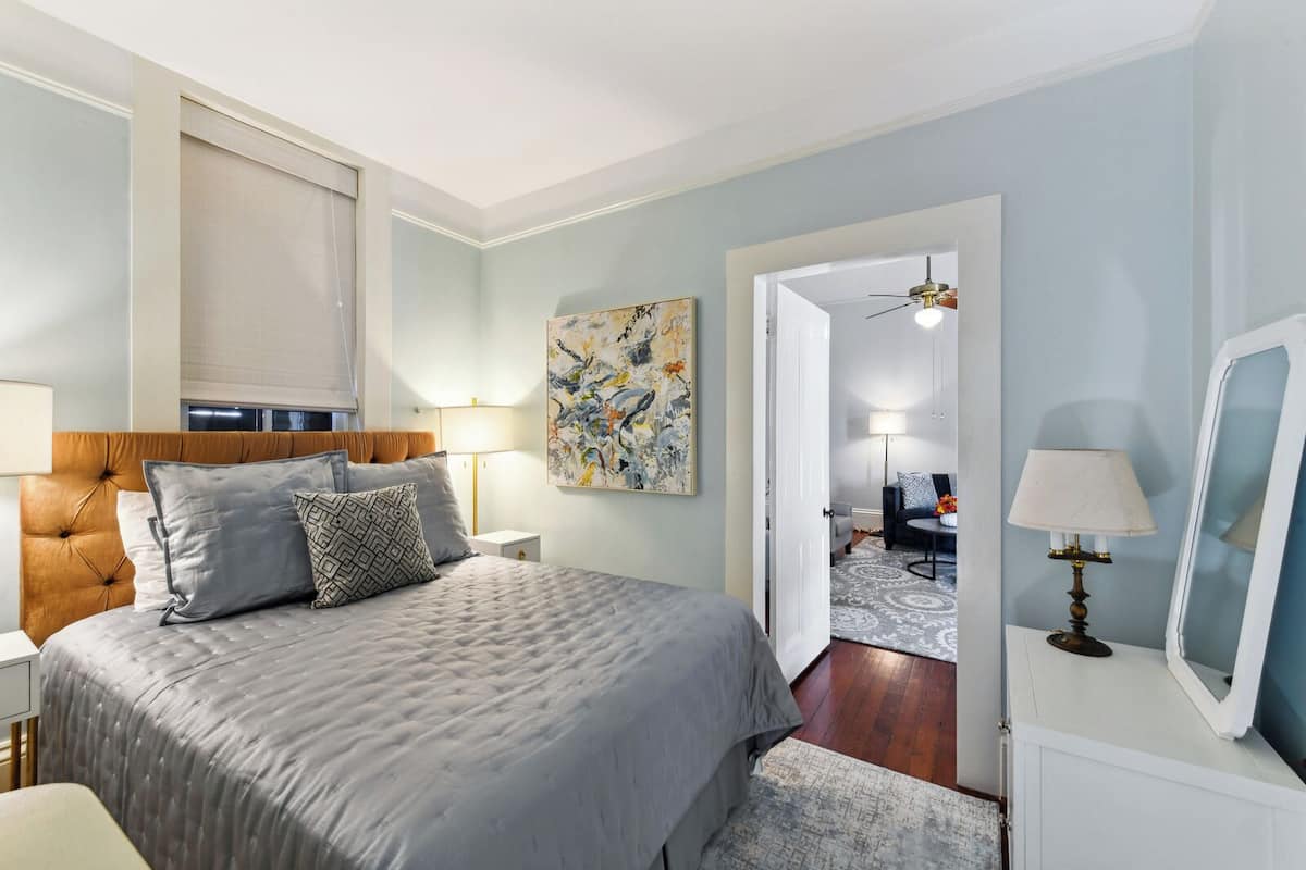 Un dormitorio con una cama grande, mesitas de noche, ventilador de techo y vista al salón.