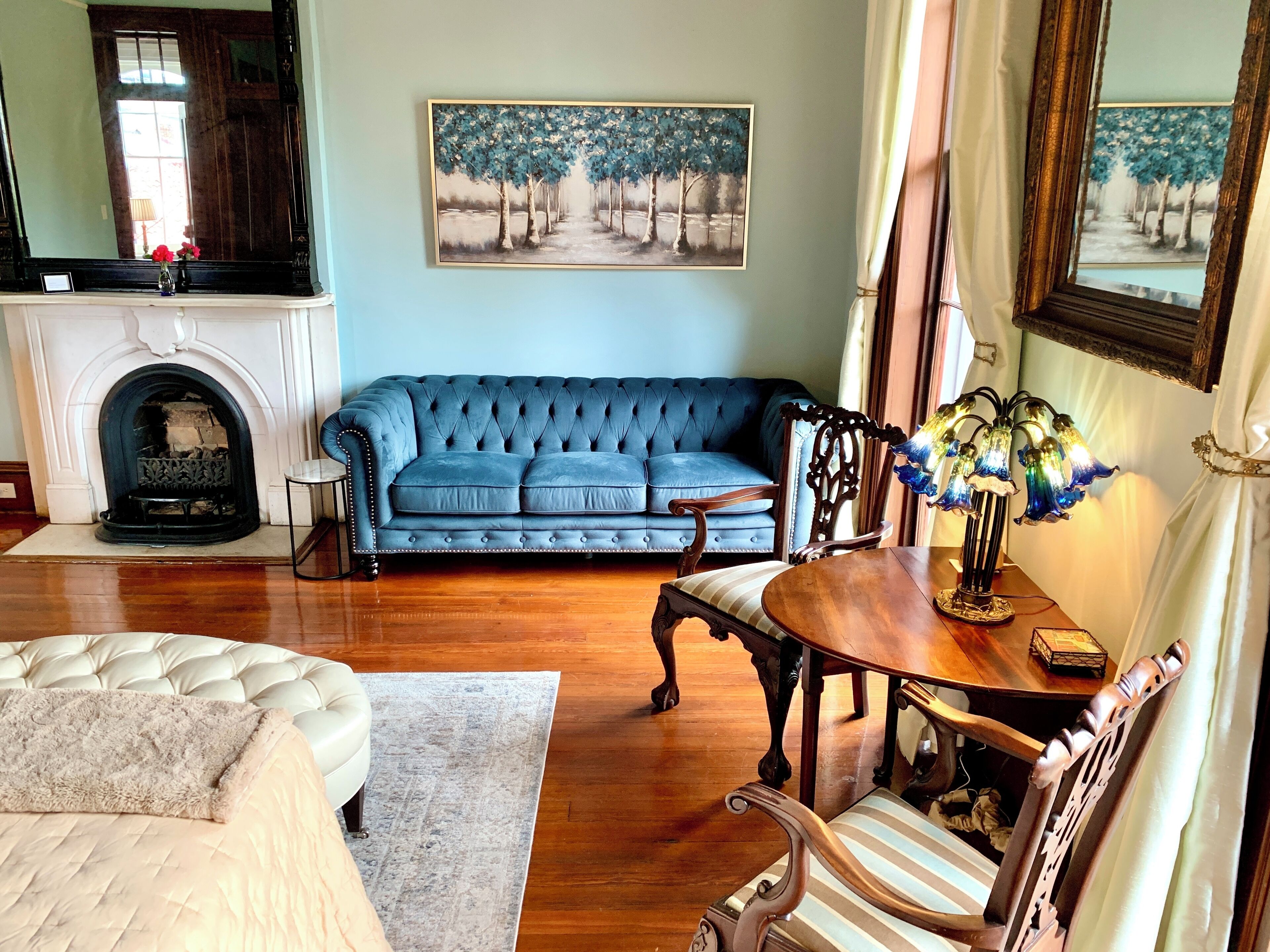 Un salón con un sofá azul, un sillón blanco, una mesa de centro de madera y una chimenea.