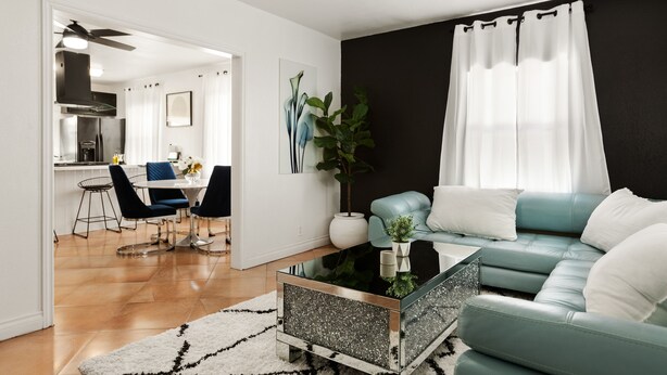 A modern living room with a teal sofa, a glass coffee table, and a dining area with blue chairs. - Prestine Pet Friendly Home near Ontario Airport- Convection Center  (Ontario)