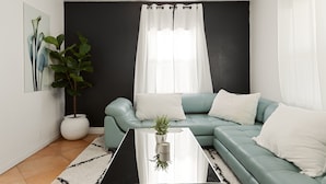 A modern living room with a teal sofa, a white coffee table, and a large potted plant. - Prestine Pet Friendly Home near Ontario Airport- Convection Center  (Ontario)