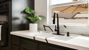 A kitchen with a white countertop, black cabinets, and a window with a view of buildings. - Prestine Pet Friendly Home near Ontario Airport- Convection Center  (Ontario)