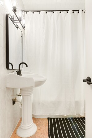 Ein Badezimmer mit einem Waschbecken auf Fuß, einem Spiegel, einer Duschvorhang und einer Streifenoptik-Bereicherung.