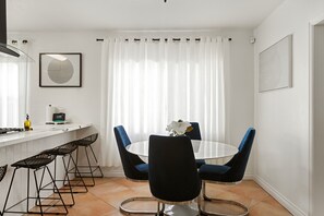 Ein moderner Essbereich mit einem runden Tisch, vier Barhocker, einer weißen Vase mit einer Blume und einem wei ßen Vorhang.
