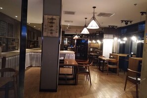 A restaurant interior with wooden flooring, tables, chairs, hanging pendant lights, and a counter area.
