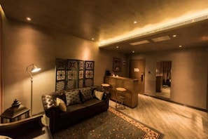 A modern living room with a sofa, a coffee table, and a patterned rug. There is a bar area with stools and a counter.