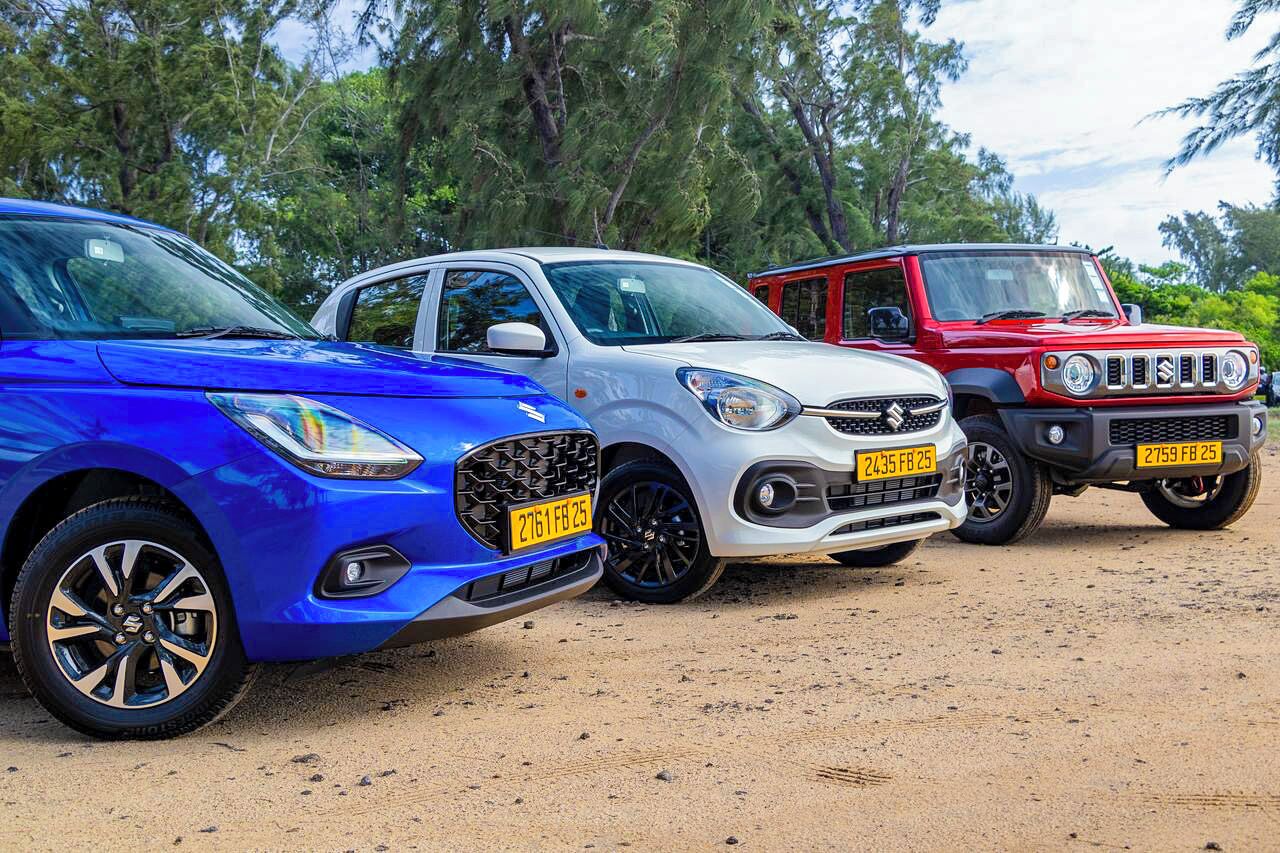 Three cars parked on a dirt surface with trees in the background.