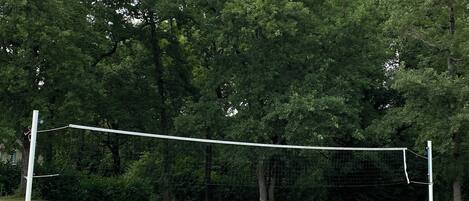 A volleyball net in a grassy field with trees in the background.