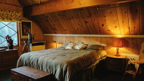 Une chambre confortable avec un plafond en bois, un grand lit recouvert d’une couvre-lit à motifs floraux, une table de chevet avec une lampe et une commode avec des tiroirs.