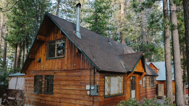 Une cabane en bois, dotée d’un toit à forte pente, entourée de grands pins.