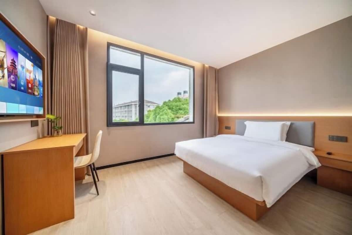 A hotel room with a bed, desk, chair, TV, and a window with a view.