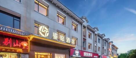 A multi-story hotel with a row of shops on the ground floor, featuring signage in a foreign script.