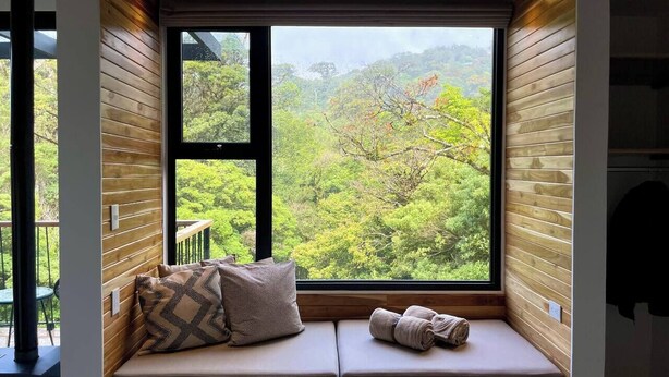 A cozy seating area with a large window offering a view of lush greenery and mountains.