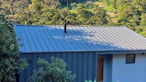 A single-story building with a corrugated metal roof, surrounded by lush greenery and hills in the background.