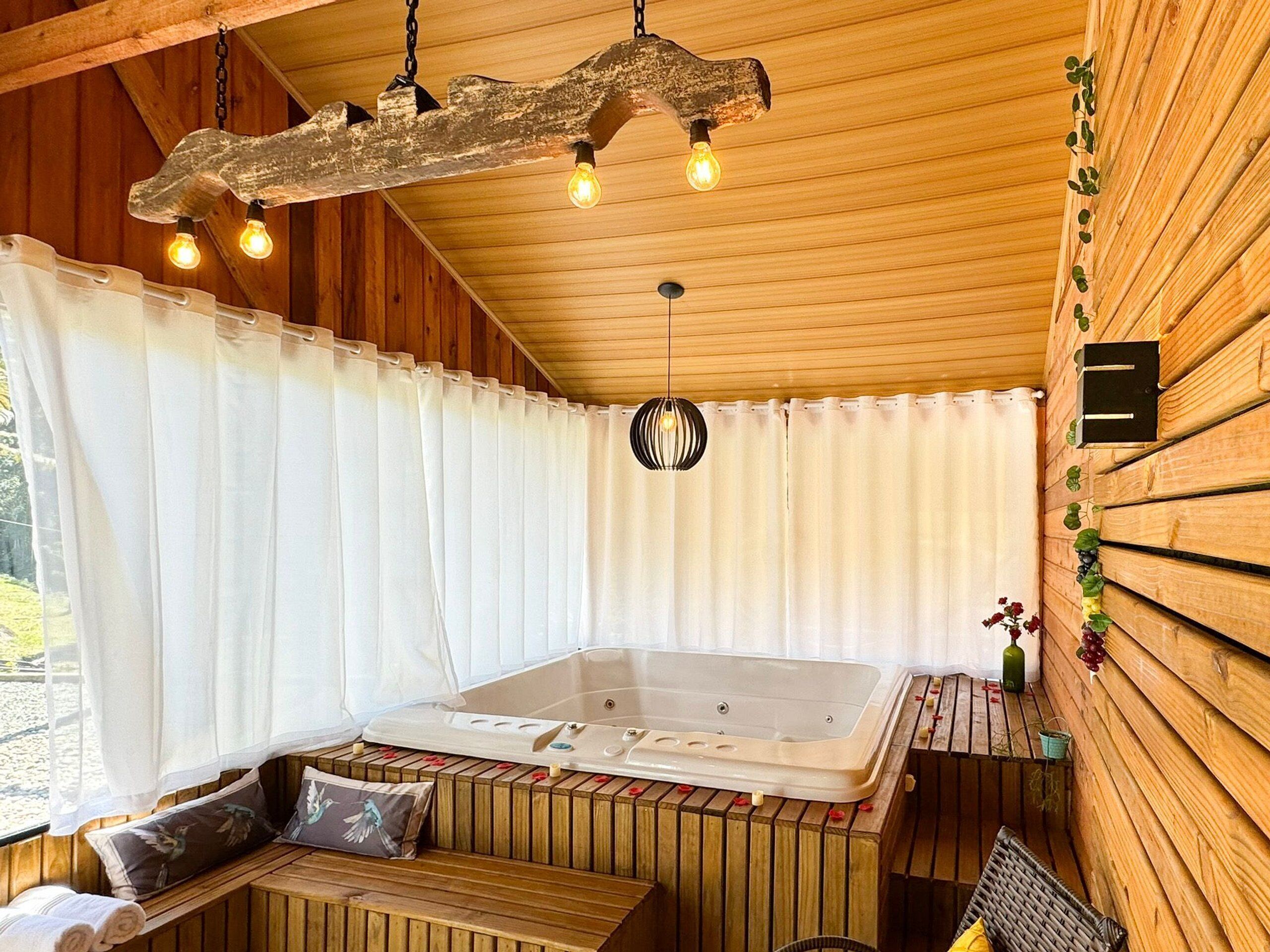 A wooden cabin with a hot tub, wooden benches, and a hanging light fixture.