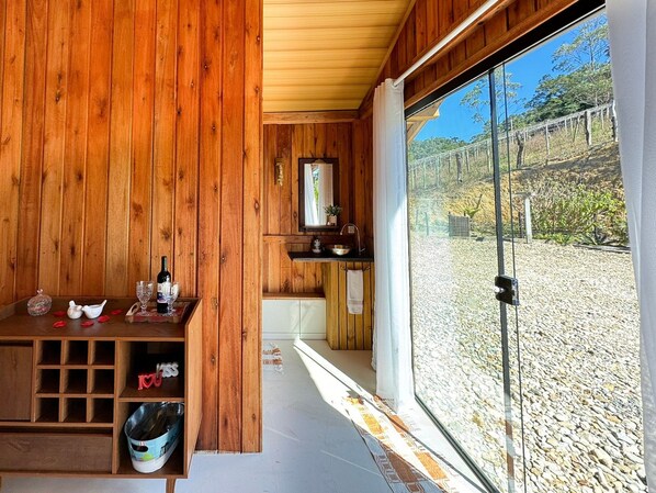 A wooden cabin with a kitchen area, a sink, and a large window overlooking a gravel path.