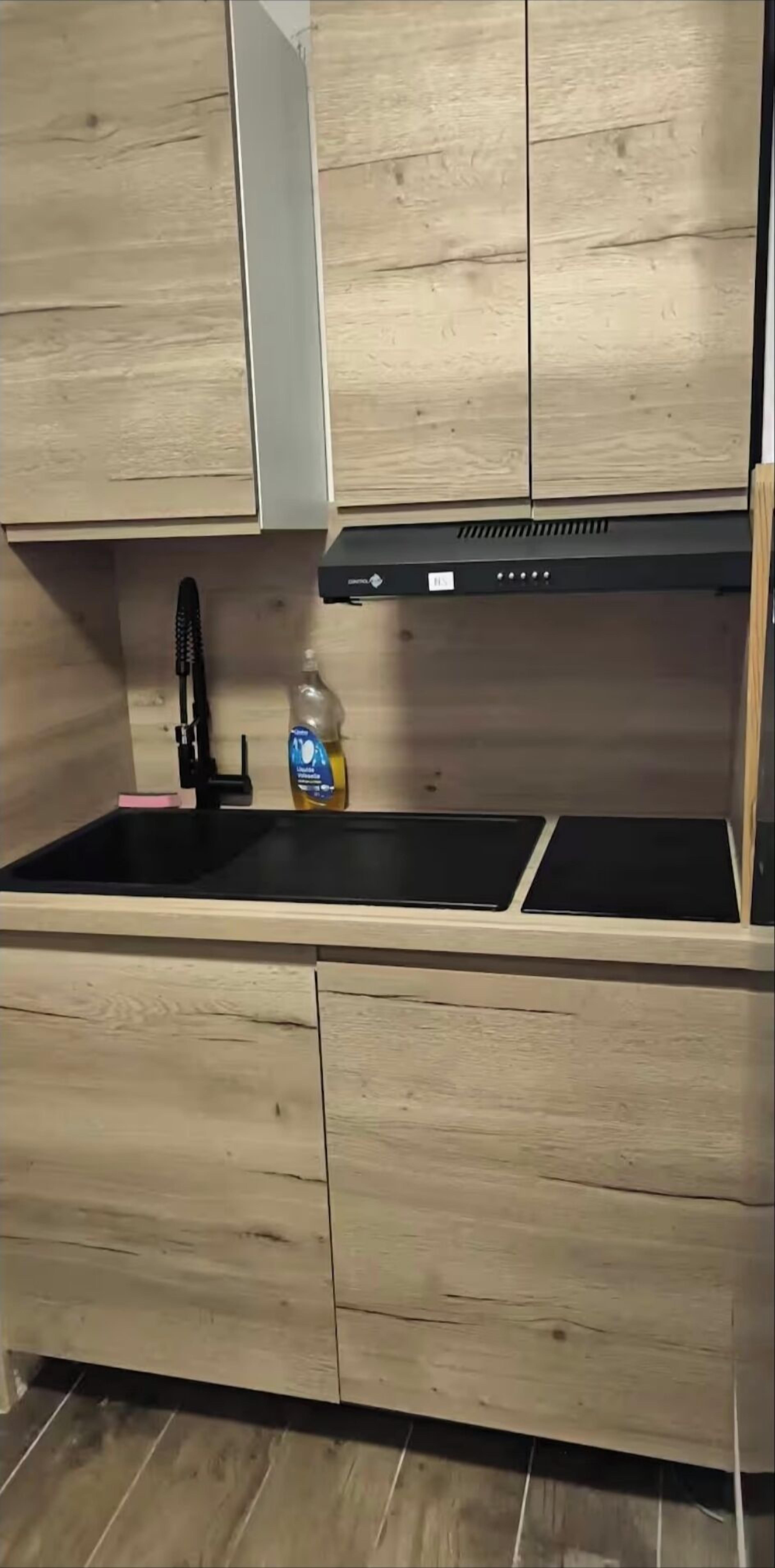 A kitchen with wooden cabinets, a black sink, and a bottle of dish soap.