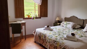 Une chambre à coucher avec un lit en bois, une table de chevet avec une lampe, une fenêtre donnant sur un paysage verdoyant et un bureau avec une chaise.